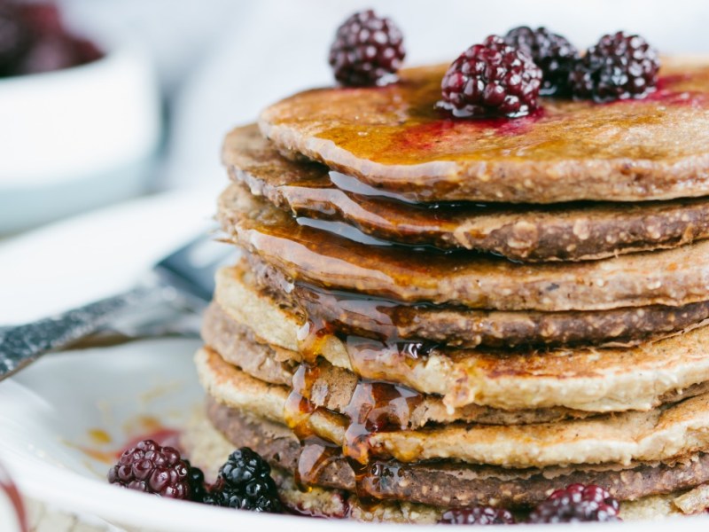 Ein Stapel Haferflocken-Pancakes mit frischen Brombeeren und Sirup.