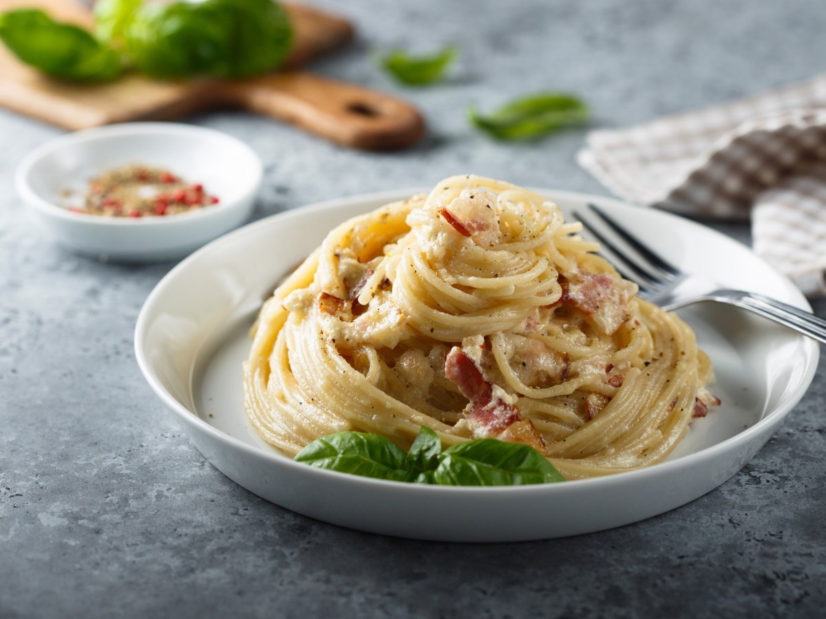 Italienische Spaghetti Carbonara auf einem weißen Teller, garniert mit Basilikum.