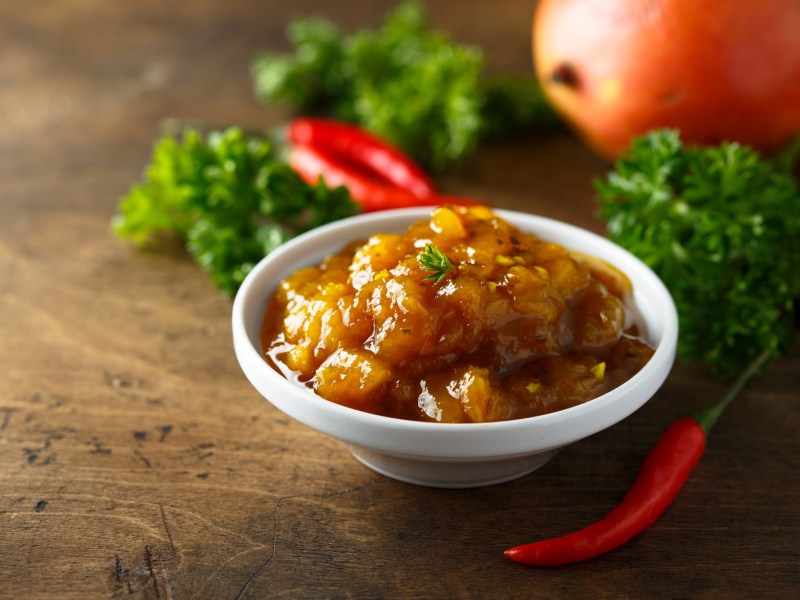 Mango-Chutney in einer kleinen Schale auf, dekoriert mit Chilis und Petersilie.