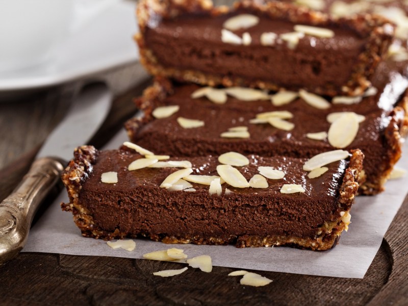 No-Bake-Schokoladentarte, bestreut mit Mandeln, in Stücke geschnitten auf einem Backpapier