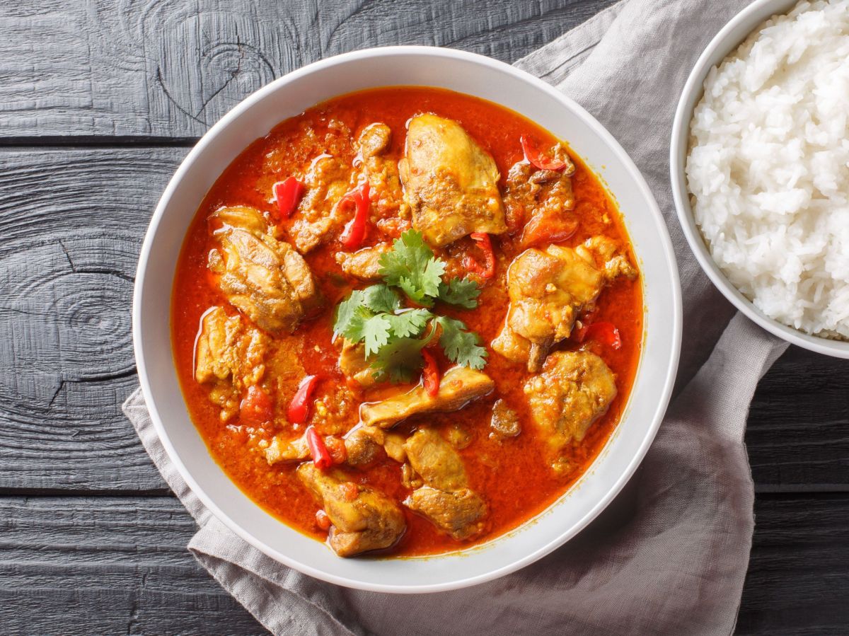 Paprika-Sahne-Hähnchen in einer Schüssel, daneben steht Reis.