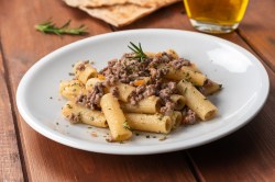 Rigatoni mit weißer Bolognese auf einem weißen Teller. Die Nudeln sind mit Kräutern dekoriert.