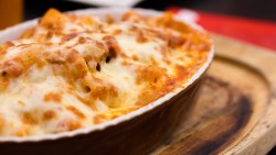 Eine Auflaufform mit Rigatoni al forno auf einem Holzbrett.