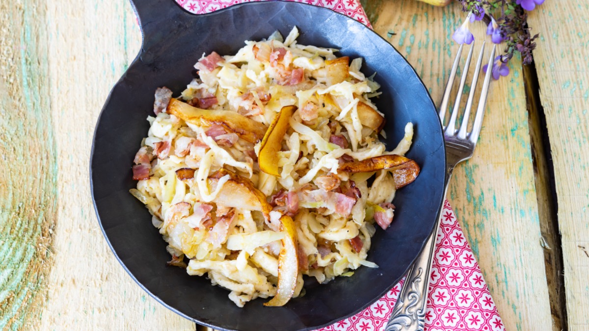 Eine Schupfnudel-Krautpfanne mit Birne und Speck von oben fotografiert. Daneben liegt eine Gabel.