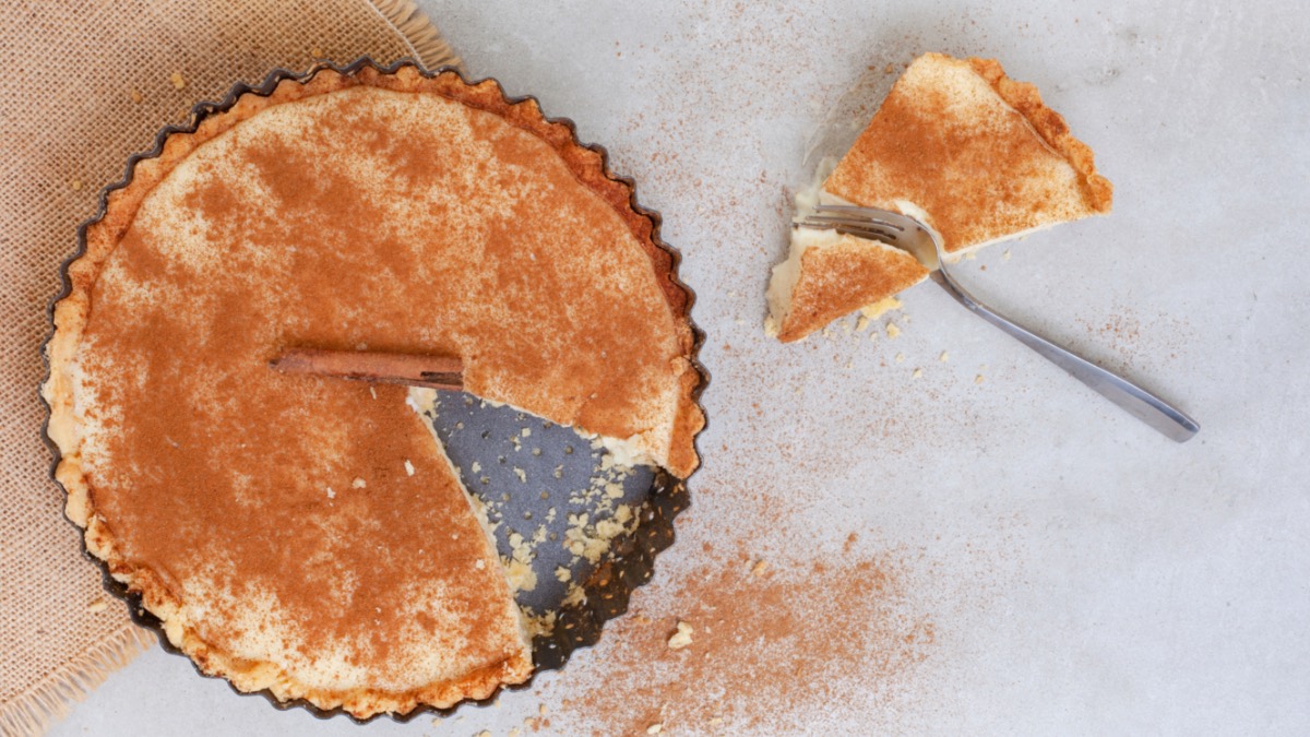 Eine südafrikanische Milchtarte in der Form, von oben fotografiert. Ein Stück Tarte liegt samt Gabel daneben.