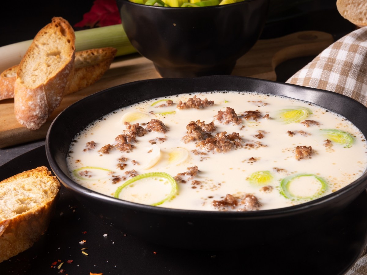 Eine Schüssel vegane Käse-Lauch-Suppe mit Hack, daneben geröstete Baguettescheiben.