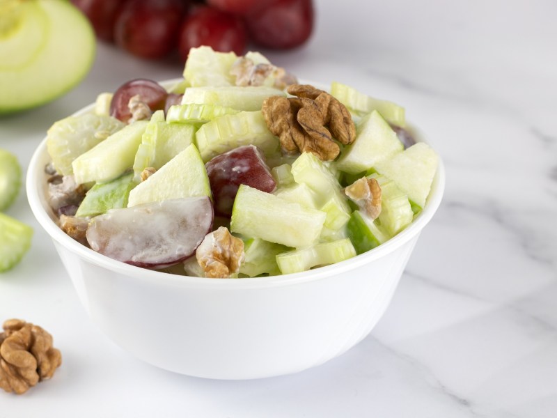 Grob geschnittener Waldorfsalat in einer weißen Schale auf einem Marmortisch.