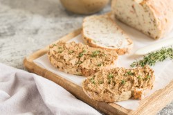 Zwei Brotscheieben mit Zwiebelbutter bestrichen auf einem Brett, auf dem auch das angeschnittene Brot liegt.