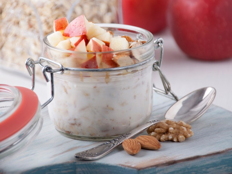 Ein Glas mit Deckel und Bircher Müsli auf einem hellen Tisch.