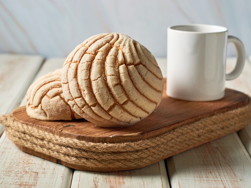 Mexikanische Conchas auf einem Holzbrett neben einer weißen Tasse