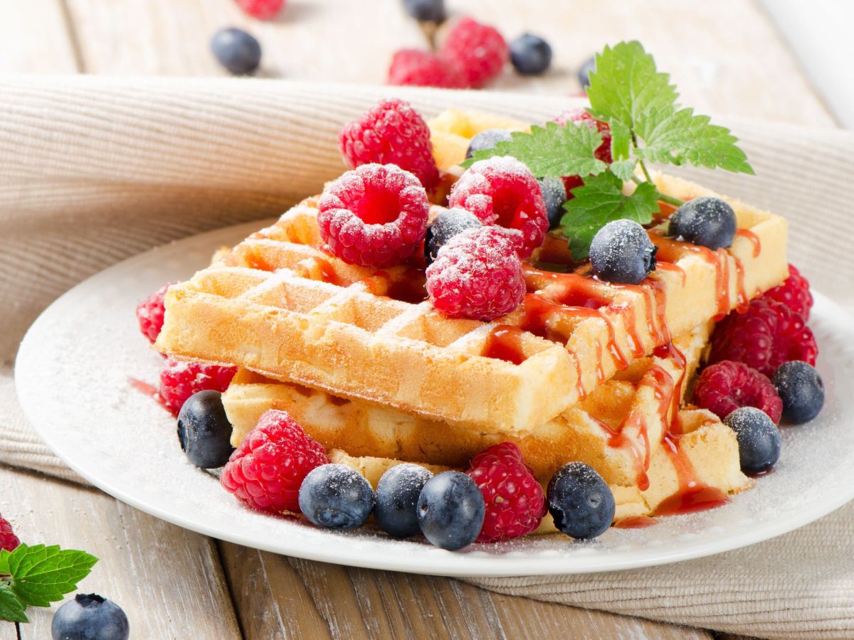 Fantakuchen-Waffeln, auf einem Teller gestapelt. Frische Beeren und ein Minzeblättchen dienen als Deko.