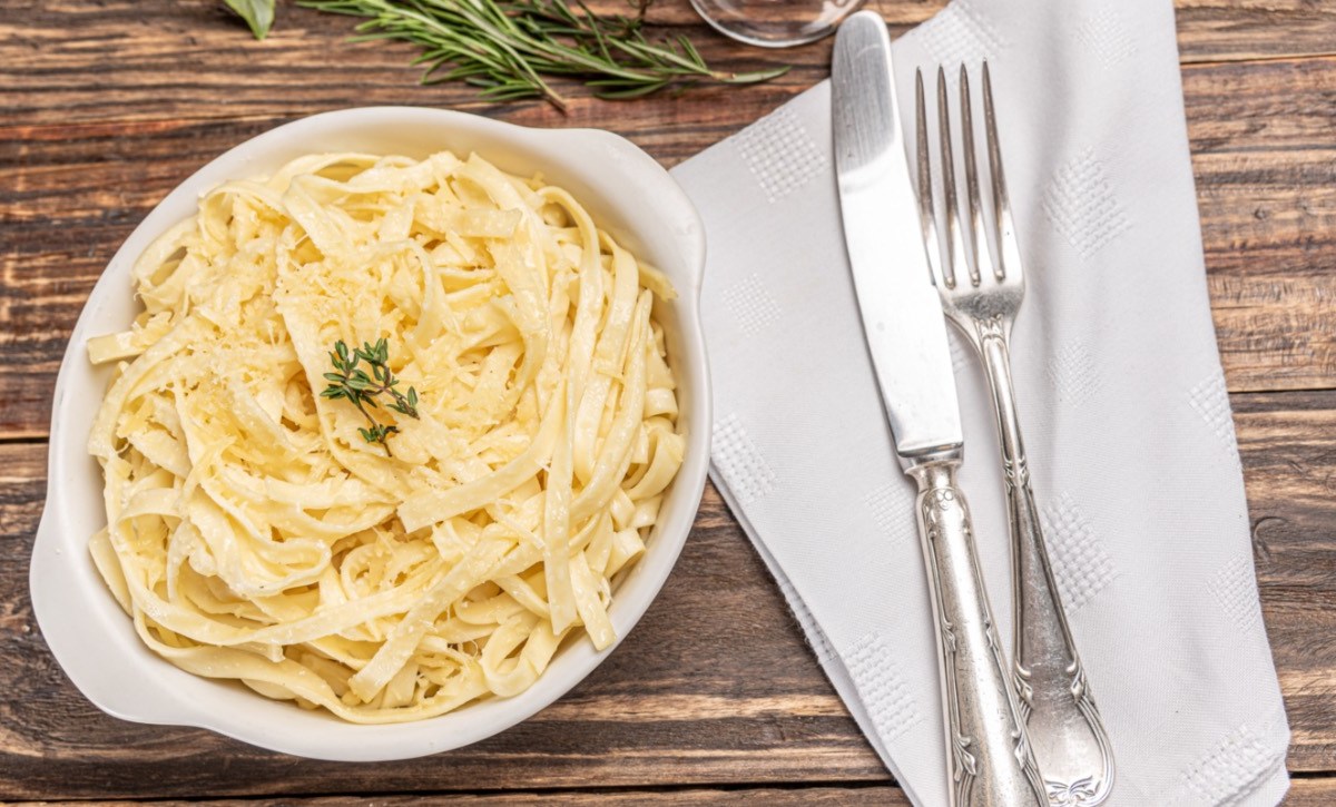 Eine Portion Fettucine Alfredo. Daneben liegt Besteck auf einer Serviette.