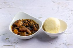 Eine Schüssel mit Fufu, einem Kloß aus Afrika, daneben eine Schüssel mit Spinateintopf.