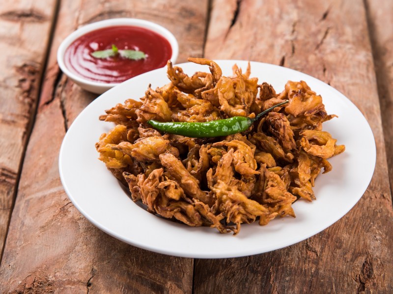 Indische Gemüsekrapfen auf einem weißen Teller, dekoriert mit einer grünen Chili und serviert mit einer roten Soße.