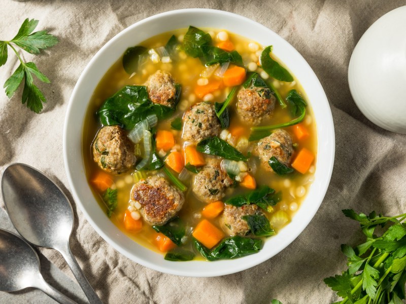 Eine Schale mit einer klaren Suppe und Einlage aus Hackbällchen, Möhren und kleinen Nudeln auf hellem Untergrund