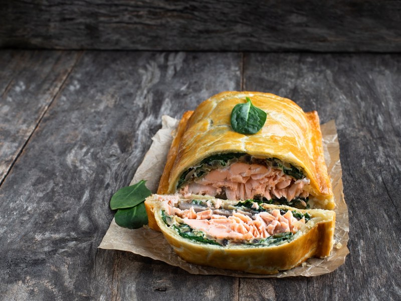 Lachs im Blätterteig mit Spinat undPilzen auf einem Stück Backpapier, garniert mit Blabyspinat.