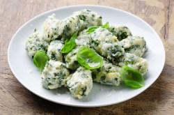 Malfatti mit Spinat und Ricotta auf einem weißen Teller, mit Basilikum garniert.