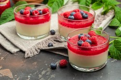 Panna Cotta mit Beerensoße und frischen Beeren garniert in kleinen Gläsern.