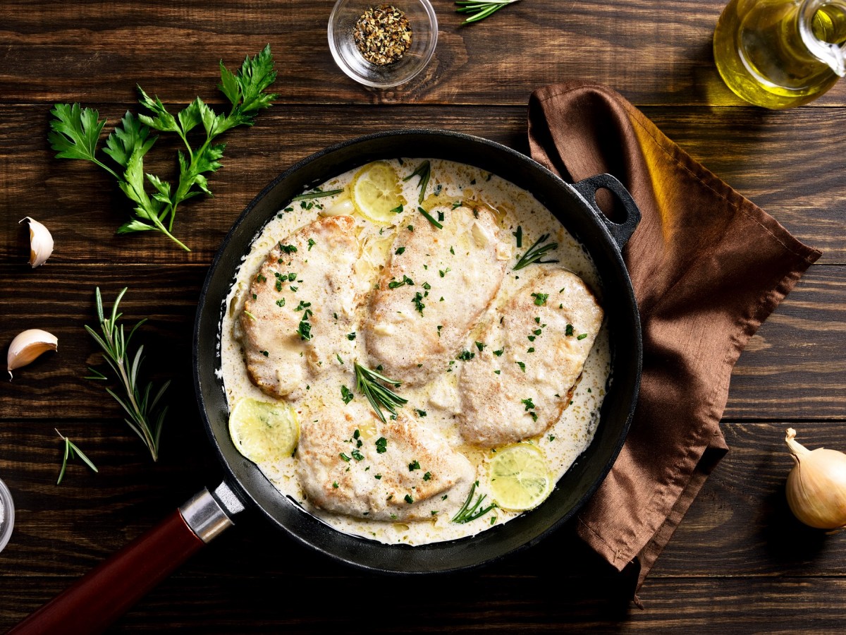 Rosmarinhähnchen in einer Pfanne auf einem braunen Tuch , umgeben von Kräutern und Zwiebeln.