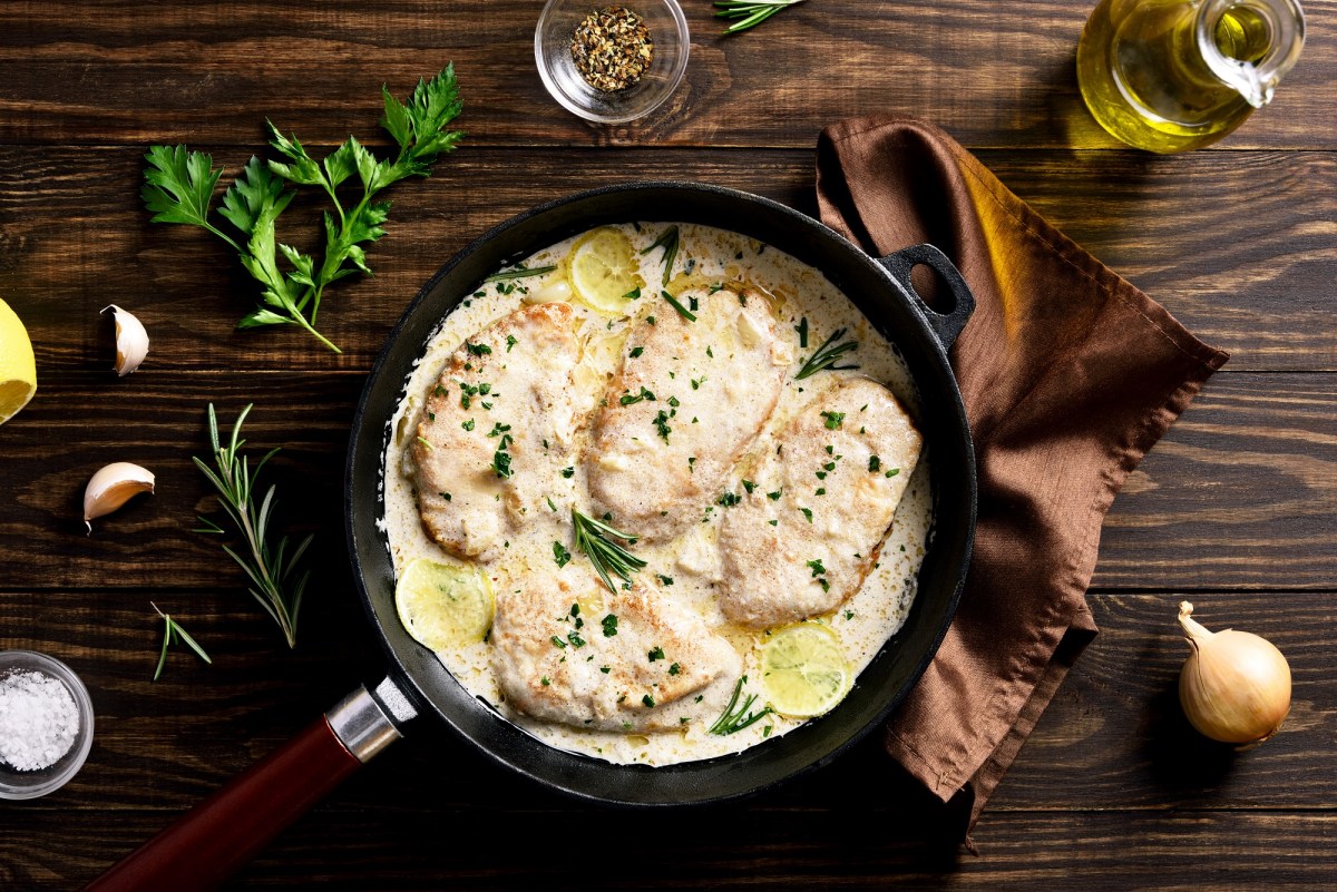 Rosmarinhähnchen in einer Pfanne auf einem braunen Tuch , umgeben von Kräutern und Zwiebeln.