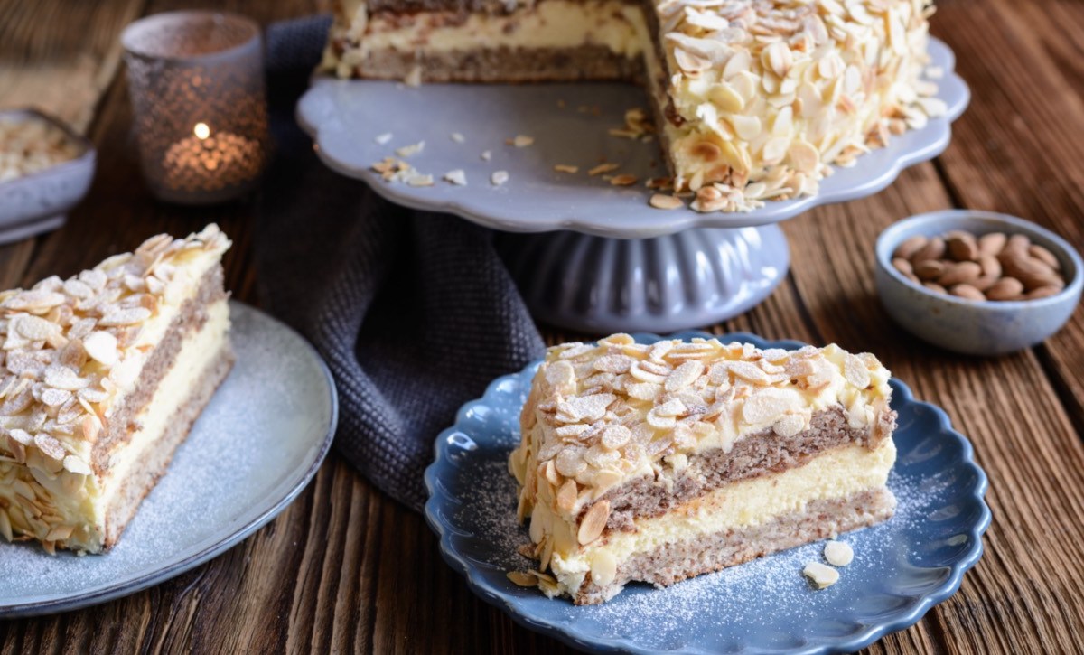 Zwei Stücke schwedische Mandeltorte auf Tellern im Vordergrund. Dahinter die restliche Torte auf einer Kuchenplatte.