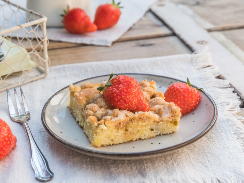 1 Stück Streuselkuchen mit Pudding garniert mit Erdbeeren auf einem Teller