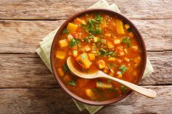 Eine Schüssel Süßkartoffel-Curry-Suppe mit Holzlöffel in der Draufsicht.