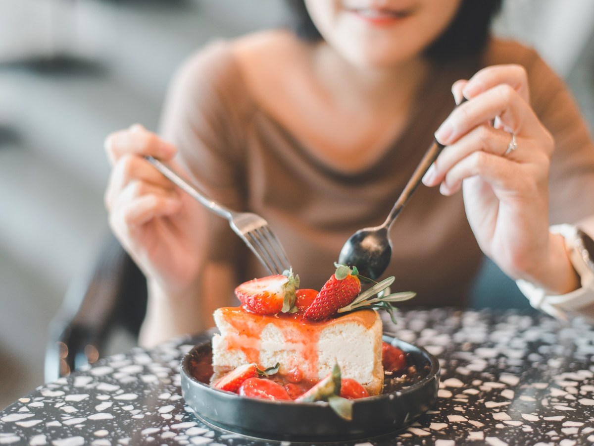 Unterschied Käsekuchen und Cheesecake: Eine Frau isst ein Stück Cheesecake mit Erdbeeren.