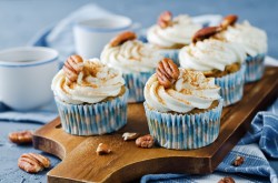 Mehrere Zimtschnecken-Cupcakes mit Zimt und Pekannüssen verziert, sie stehen auf einem Brett.