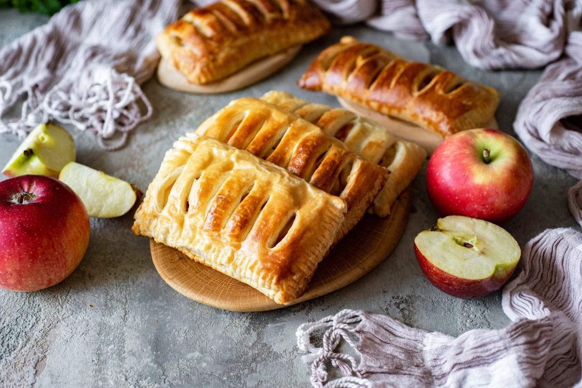 4 Apfel-Quark-Taschen auf einem Teller, drumherum ganze und halbierte Äpfel.