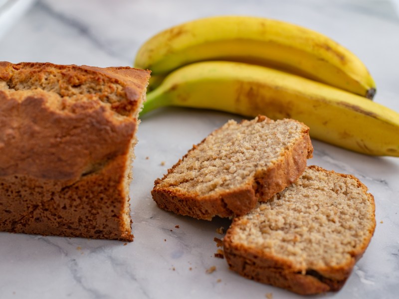 Ein angeschnittenes Bananenbrot ohne Zucker, daneben zwei Bananen.