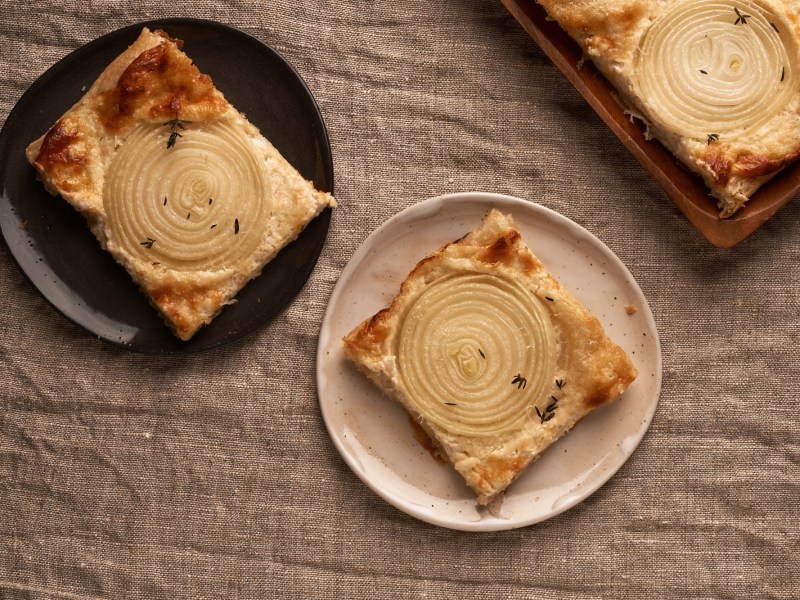 zwei Teller mit Zwiebel-Tartelettes auf braunem Leinentuch