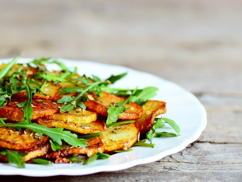 Ein Teller Bratkartoffeln mit Rucola und Knoblauch, Nahaufnahme