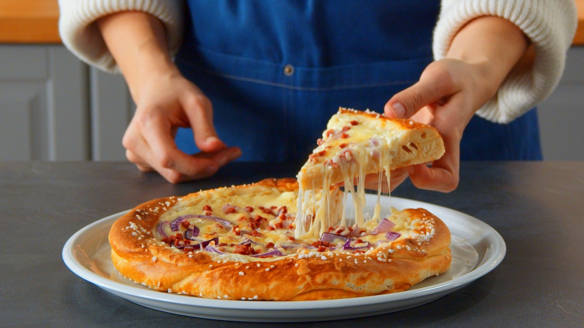 Eine Brezelpizza, von der eine Frau ein Stück nimmt.