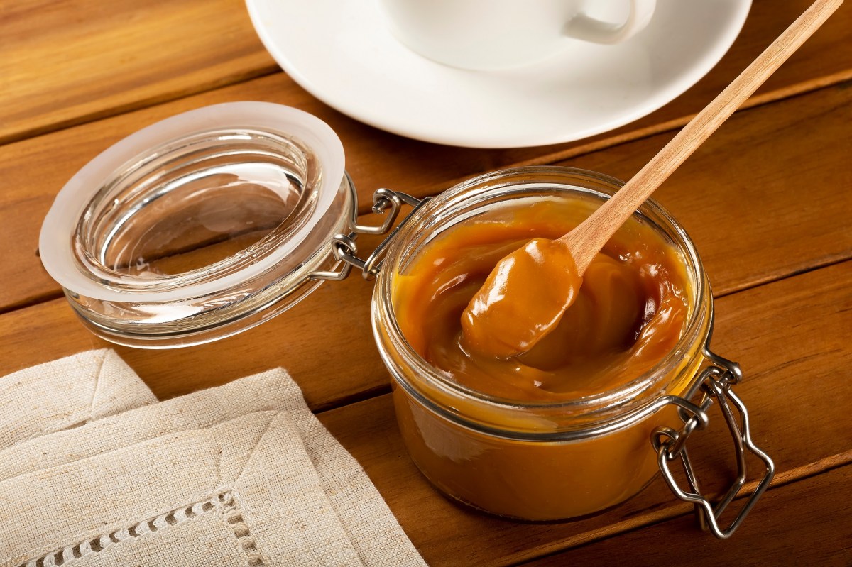 Dulce de Leche in einem Glas mit Deckel auf einem Tisch neben einer Zeitung.