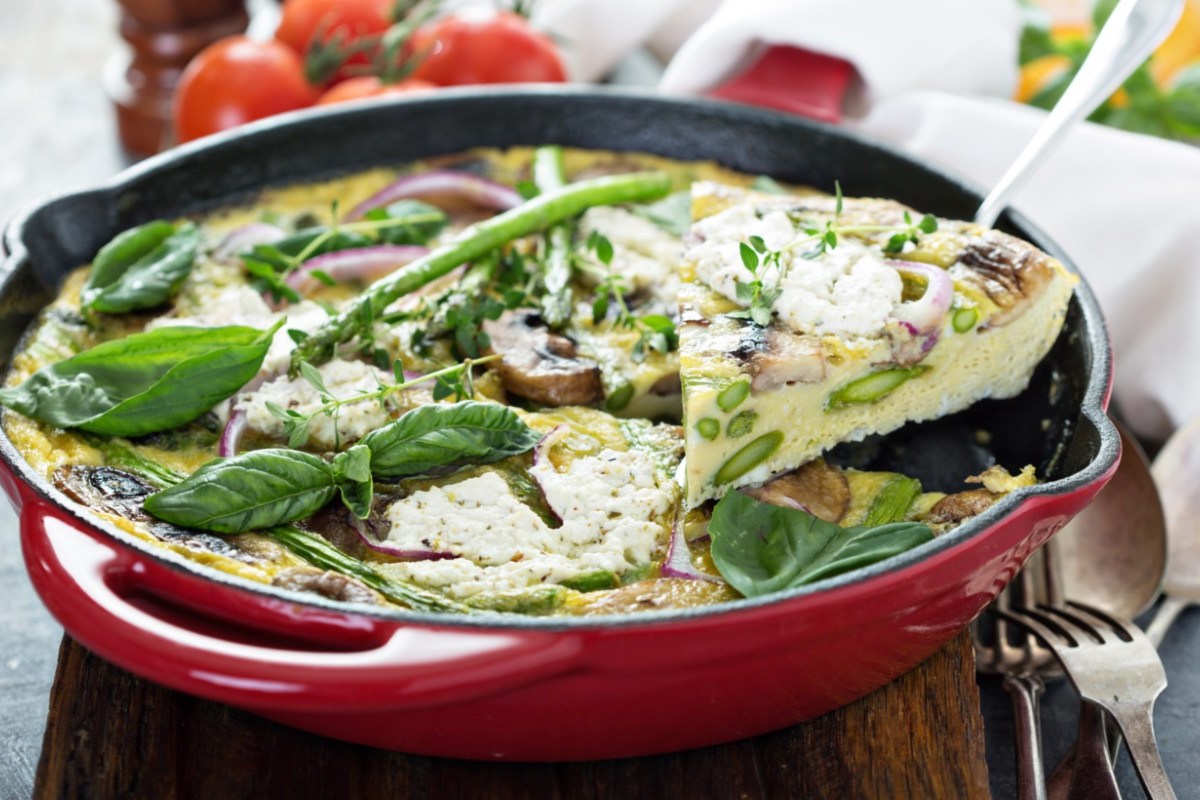 Eine Frittata mit Ziegenkäse und Spargel in einer roten Pfanne. Ein Stück wird gerade entnommen.