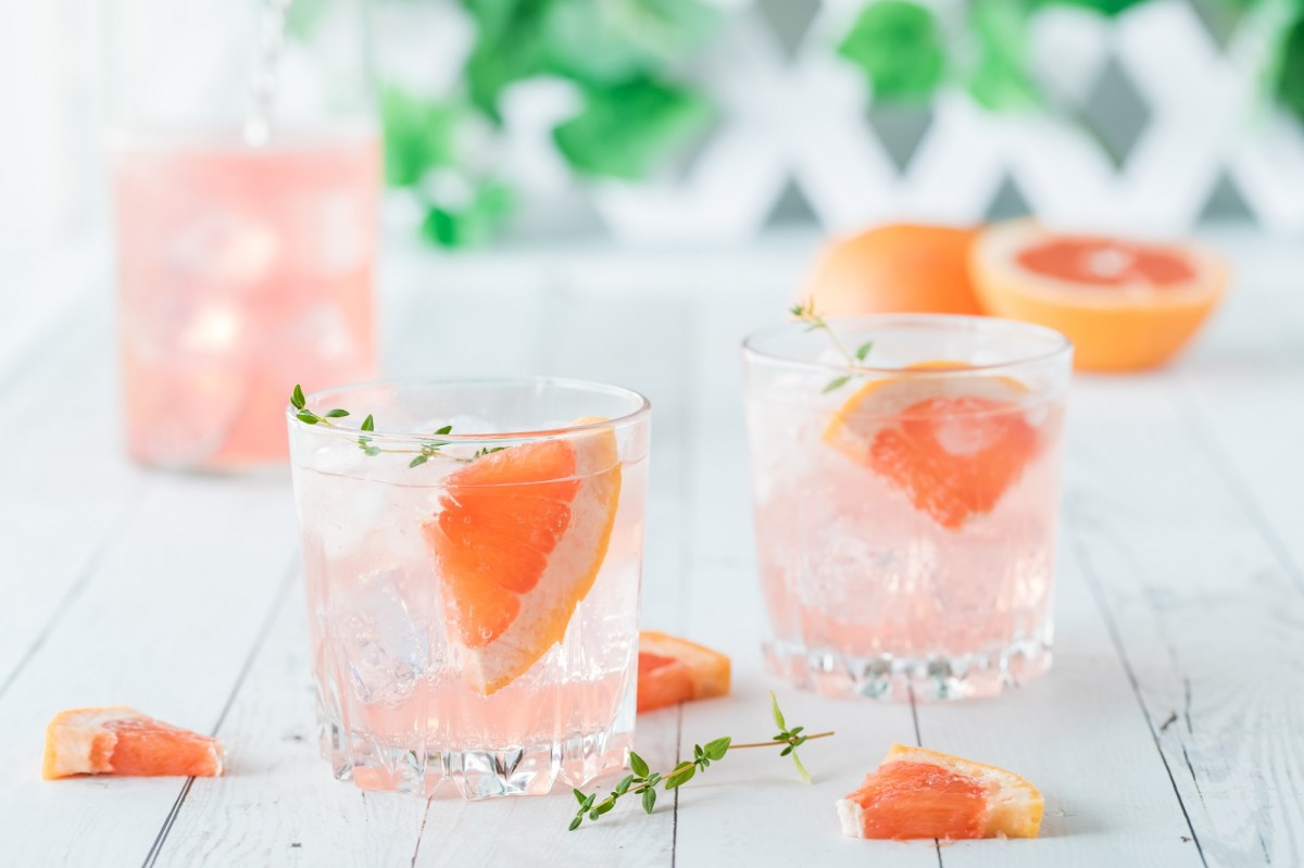 Drei Gläser Grapefruit Fizz mit halben Grapefruits auf hellem Untergrund.