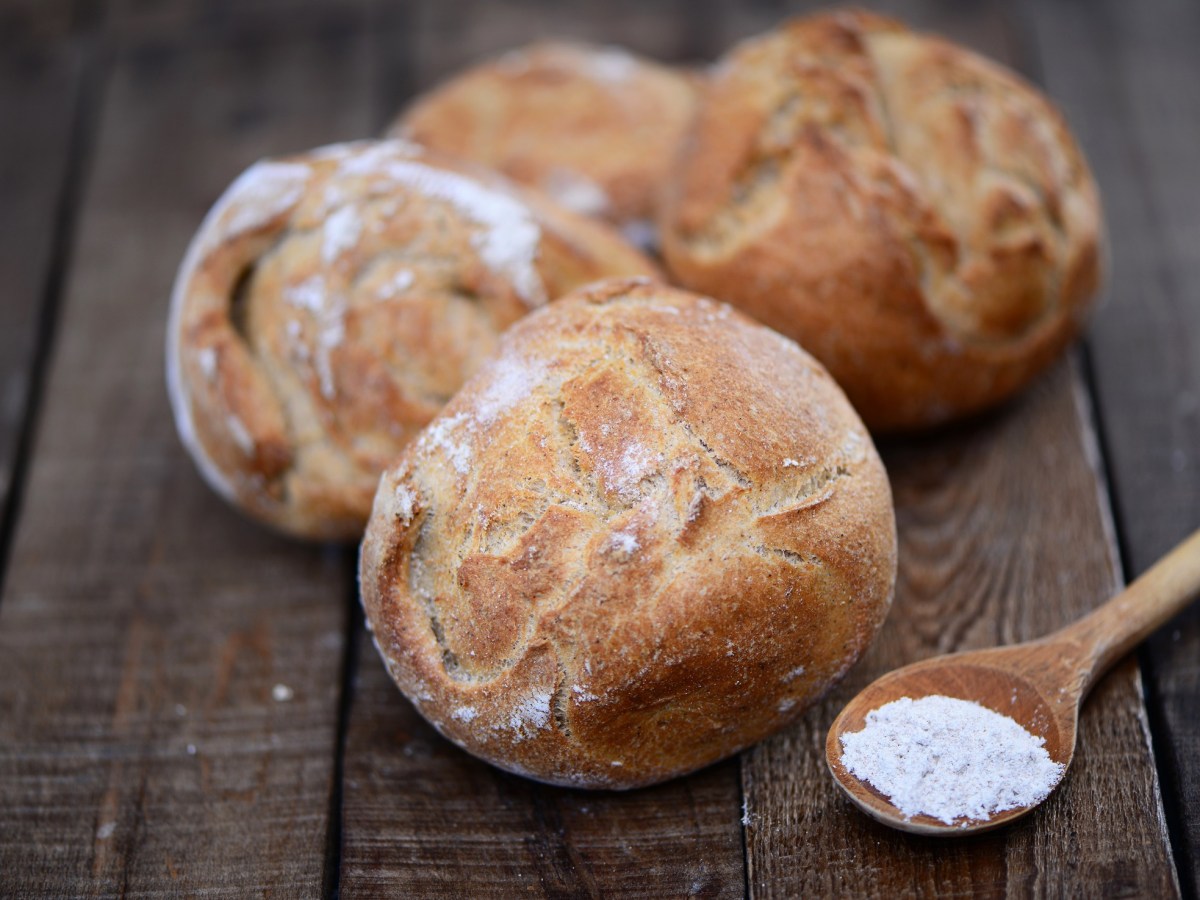 selbst gebackene Kartoffel-Brötchen mit Löffel Mehl auf Holztisch