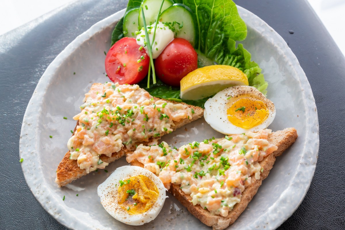 Ein Teller mit zwei Toastscheiben mit Lachs-aufstrich, Tomaten und zwei halben Eiern.