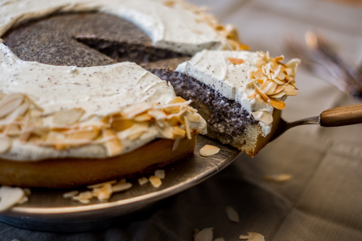 Mohnkuchen mit Birnen und Quark sowie Mandeln, aus dem ein Stück mit einem Tortenheber herausgenommen wird.