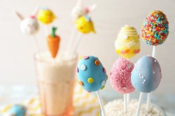 Bunte Oster-Cakepops am Stiel, verziert mit Zuckerperlen, im Hintergrund unscharf weitere Cakepops.