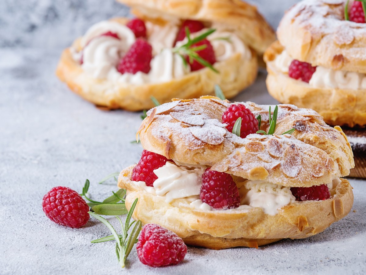 Drei kleine Paris-Brest, mit Himbeeren und Rosmarin garniert.