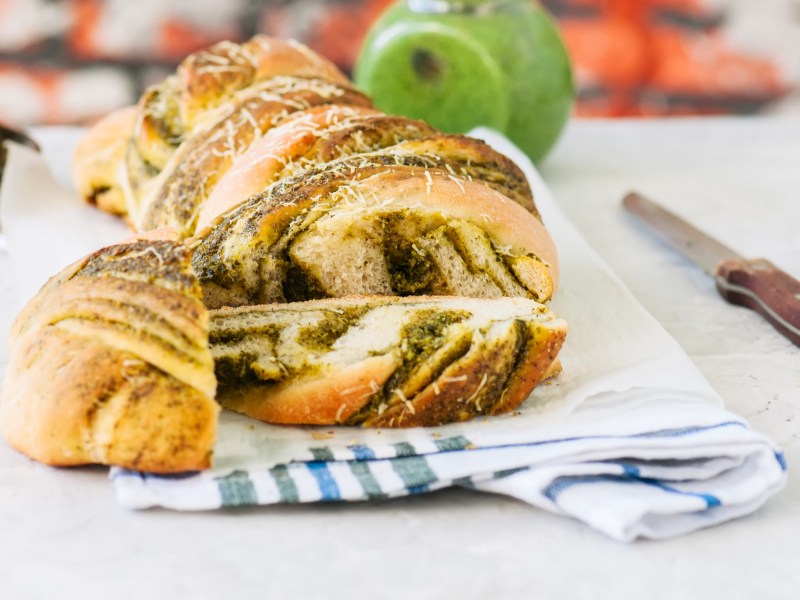 ein angeschnittenes Pestobrot mit Parmesan auf einem Geschirrtuch, daneben ein Messer.