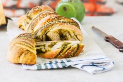 ein angeschnittenes Pestobrot mit Parmesan auf einem Geschirrtuch, daneben ein Messer.