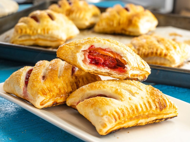 Mehrere Pizzataschen aus Blätterteig gefüllt mit Tomatensoße, Gemüse und Käse.