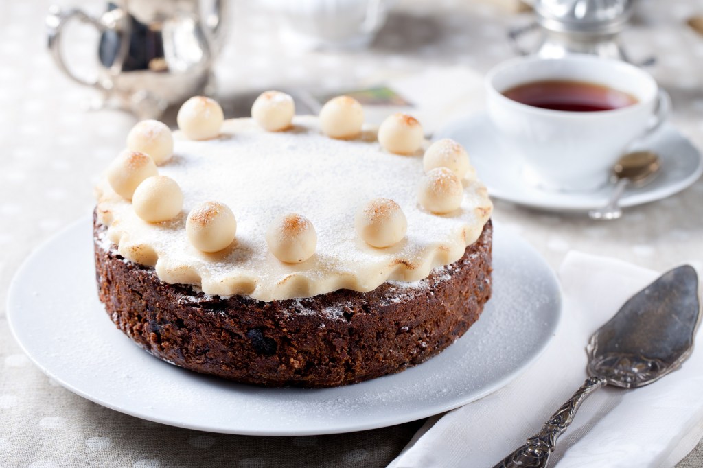 Ein Simnel Cake auf einer Kuchenplatte, daneben eine Tasse Tee und ein Tortenheber.