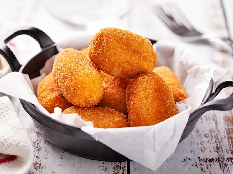 Spanische Kroketten in einem gusseisernen Topf auf einem Holztisch.