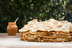 Tausend-Blatt-Torte mit Blätterteig und Baoserhaube auf einem Tisch. Daneben unscharf im Hintergrund ein Glas Dulce de Leche.