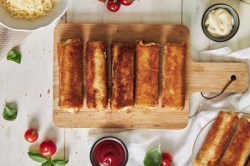 Fünf Toast-Röllchen auf einem Holzbrett. Drumherum stehen Schalen mit Dip und frische Zutaten.