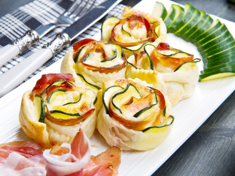 Fünf Zucchini-Blätterteig-Rosen auf einer eckigen Servierplatte.